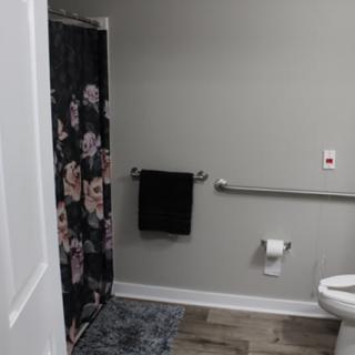 A modern bathroom with a floral shower curtain, toilet, and black towel on a rack.