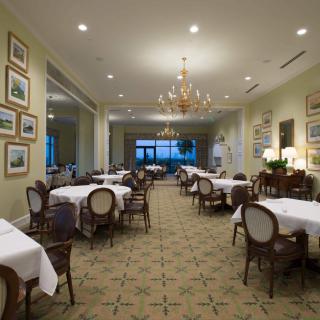 A well-lit, elegant dining room with neatly arranged tables and chairs, adorned with chandeliers and artwork on the walls.