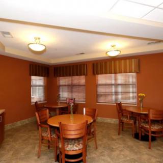 A cozy room with round wooden tables and chairs, featuring warm lighting and windows with striped curtains.