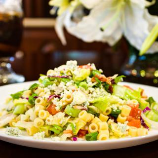 A colorful pasta salad with fresh vegetables and cheese on a white plate.