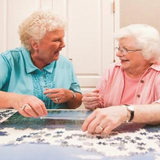 Two senior women enjoying a puzzle together and sharing a laugh.