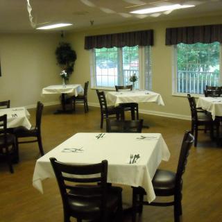 An empty dining room with neatly set tables and chairs, featuring windows with curtains.