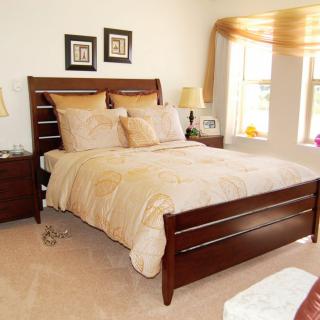 A cozy and well-decorated bedroom with a wooden bed, matching nightstands, and a sunlit window.