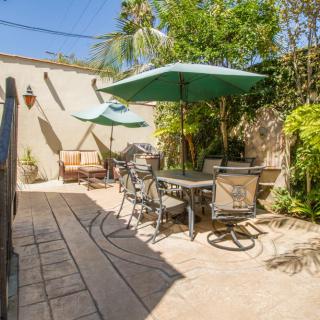 A sunny patio with outdoor furniture and umbrellas, surrounded by lush plants.