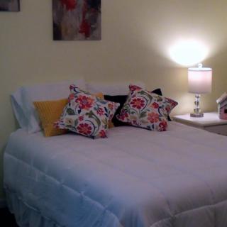 A cozy bedroom with a neatly made bed adorned with floral patterned pillows and a softly lit lamp on the nightstand.
