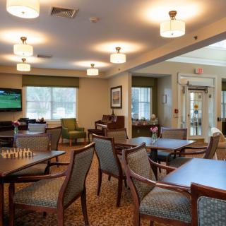 A cozy dining area with multiple tables and chairs, well-lit by ceiling lights, featuring a television and large windows.