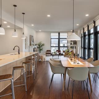 A modern open-concept kitchen and dining area featuring an island with stools, pendant lighting, and hardwood floors.