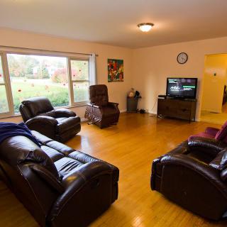 A cozy living room with leather sofas and a TV, featuring large windows that let in natural light.