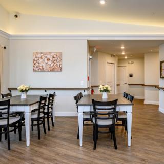 A modern dining area with neatly arranged tables, black chairs, and floral centerpieces against a backdrop of light-colored walls and wooden flooring.