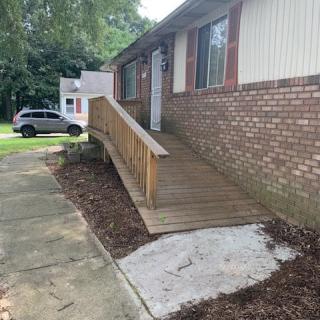 A wooden accessibility ramp leading to the entrance of a brick house.