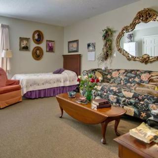 A cozy, vintage-style living and bedroom space with a floral sofa, large mirror, and decorative portraits.