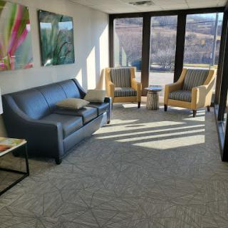 A cozy and well-lit office waiting area featuring a gray sofa and yellow armchairs.