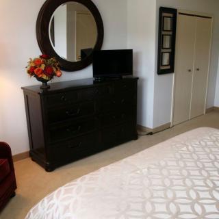 A cozy bedroom with a dresser topped by a round mirror, a television, and decorative flowers.