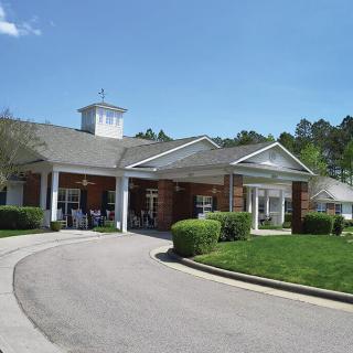 A building with a covered entrance and circular driveway, surrounded by well-maintained landscaping.