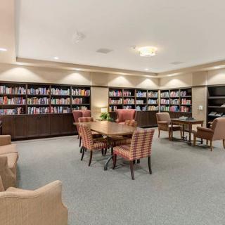 A cozy library reading area with bookshelves, comfortable chairs, and tables.