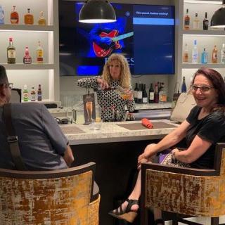 People enjoying drinks at a bar with a bartender serving and a TV in the background.