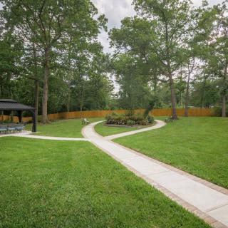 A serene garden with a winding pathway, surrounded by lush trees and a wooden fence.