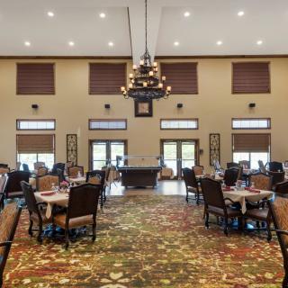 An elegant dining room with neatly arranged tables and chairs, featuring a central chandelier and large windows.