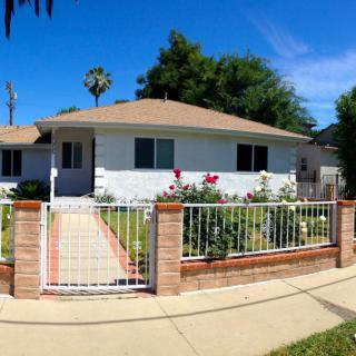 A suburban home with a garden and white fence on a sunny day.