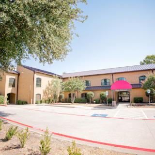 A view of a hotel building with a welcoming entrance and well-maintained landscaping under clear blue skies.