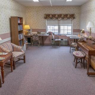 A cozy office space featuring a piano, desk, bookshelf, and seating area.