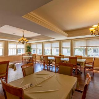 A well-lit restaurant dining room with neatly arranged tables and chairs next to large windows.