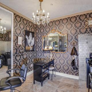 An elegant salon interior featuring luxurious wallpaper, a chandelier, and mirrored walls.