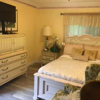 A cozy bedroom featuring a bed, dresser with a TV on top, and a lamp next to the window.