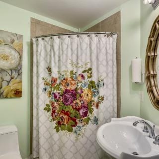 A cozy bathroom with a floral shower curtain, pastel green walls, and decorative artwork.