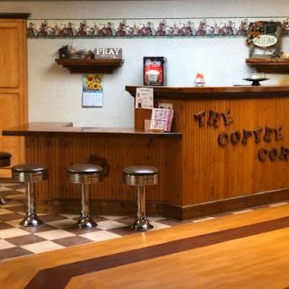 A cozy coffee shop interior featuring a wooden counter and bar stools complemented by a checkered floor.