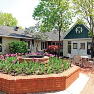 A charming garden with a brick planter filled with flowers, surrounded by outdoor seating and trees.