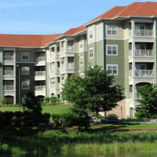 A modern apartment building with a green facade and red roof, surrounded by landscaping and trees.