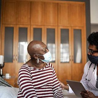 A doctor in a mask consulting with a patient in a hospital room.
