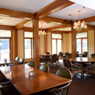 A spacious restaurant dining area featuring wooden tables and chairs, elegant chandeliers, and large windows.