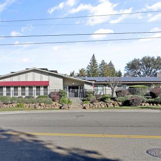 A roadside building with a red awning, trees in the background, and a clear blue sky.
