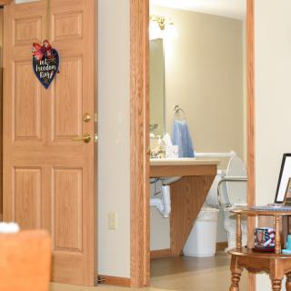 A cozy interior with a view of a wooden door leading to a bathroom featuring a mirror and sink.