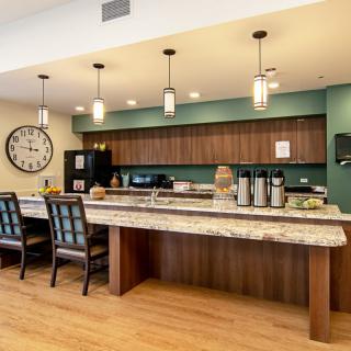 A modern kitchen area featuring a counter with chairs, pendant lights, and a coffee station.