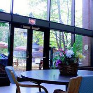 A lobby area with a round table, chairs, and a basket of flowers near large glass doors letting in natural light.