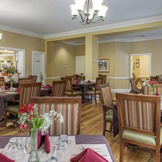 A cozy dining room with neatly set tables and comfortable chairs under a chandelier.