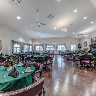 A spacious dining room with neatly arranged tables covered in green tablecloths, surrounded by comfortable chairs and well-lit by ceiling lights.