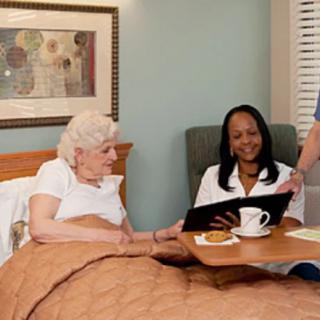 A nurse and a healthcare worker interacting with an elderly patient in a hospital room.