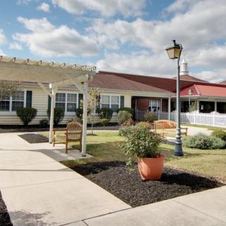 A charming building with a well-maintained garden area, featuring benches and a lamp post under a partly cloudy sky.