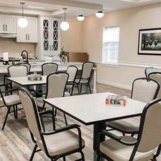 A well-lit dining area with multiple tables and chairs, adjacent to a kitchen.