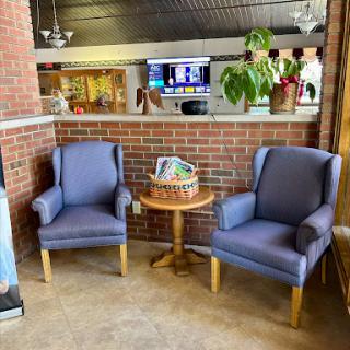 A cozy seating area featuring two blue chairs and a small table adorned with a decorative basket, set against a rustic brick wall.