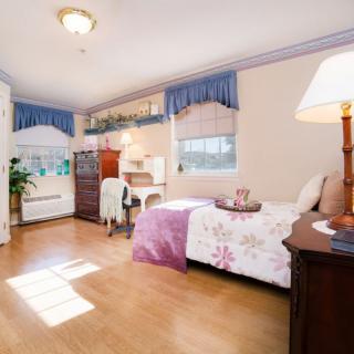 A cozy bedroom with natural light, featuring a bed, desk, and elegant furnishings.
