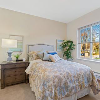 A cozy bedroom with a neatly made bed, nightstand, and a large window.
