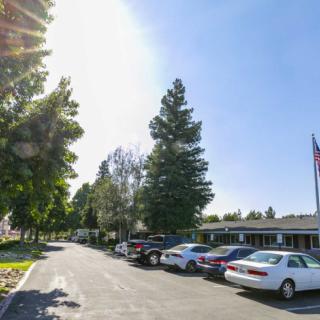 A sunny day in a parking lot lined with cars, trees, and a building with an American flag.