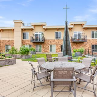 A serene outdoor seating area featuring modern furniture and lush landscaping, complemented by a striking cross sculpture.