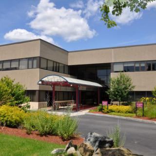 This image shows a commercial office building with a landscaped entrance under a sunny sky.