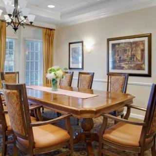A well-furnished dining room featuring a large wooden table surrounded by chairs, with artwork on the walls and a chandelier above.